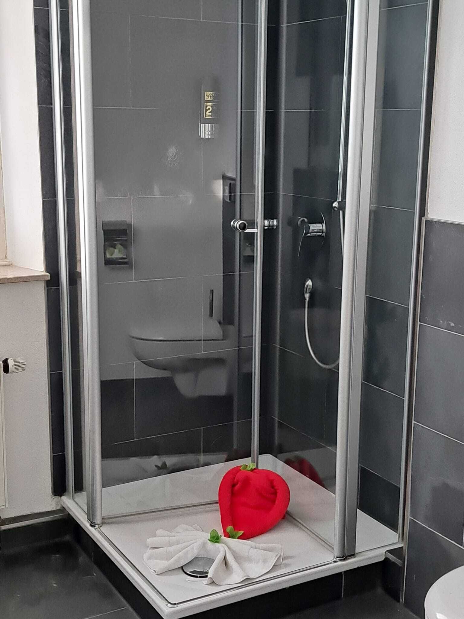 A modern bathroom with a glass-enclosed shower, a white sink, and a red heart-shaped decoration on the floor.