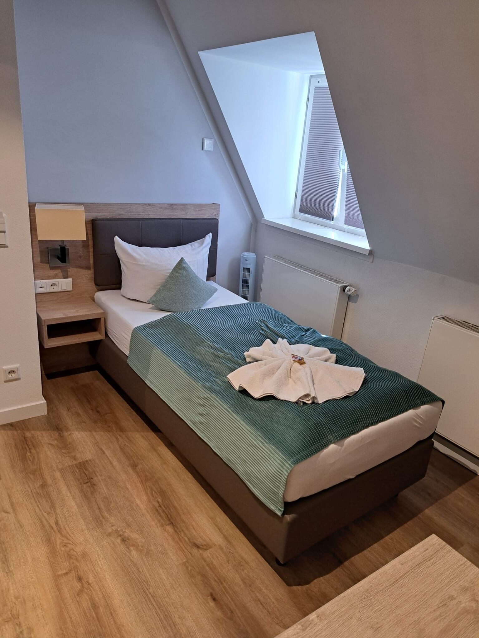 Una habitación de hotel moderna con una cama, una mesita de noche, una lámpara, una ventana y un radiador.
