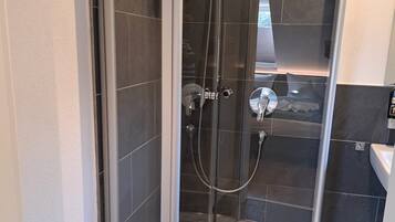 Cabina de ducha con paredes de vidrio y una toalla blanca en el suelo.