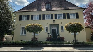 A two-story building with a symmetrical facade, a central entrance with a green door, and two trees in front. - VILLAWIE  (Rheda-Wiedenbrück)