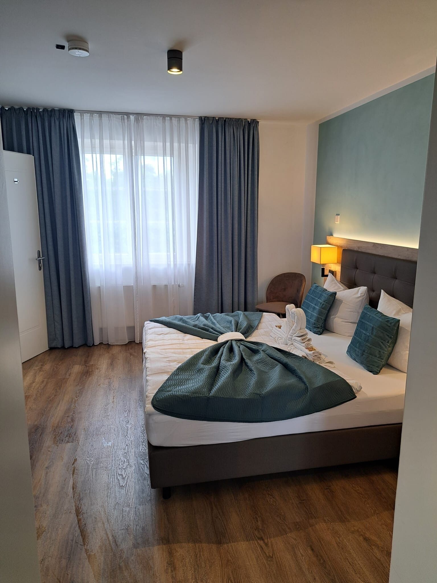 Een hotelkamer met een groot bed, een nachtkastje, een lamp en uitzicht op het landschap door het raam.