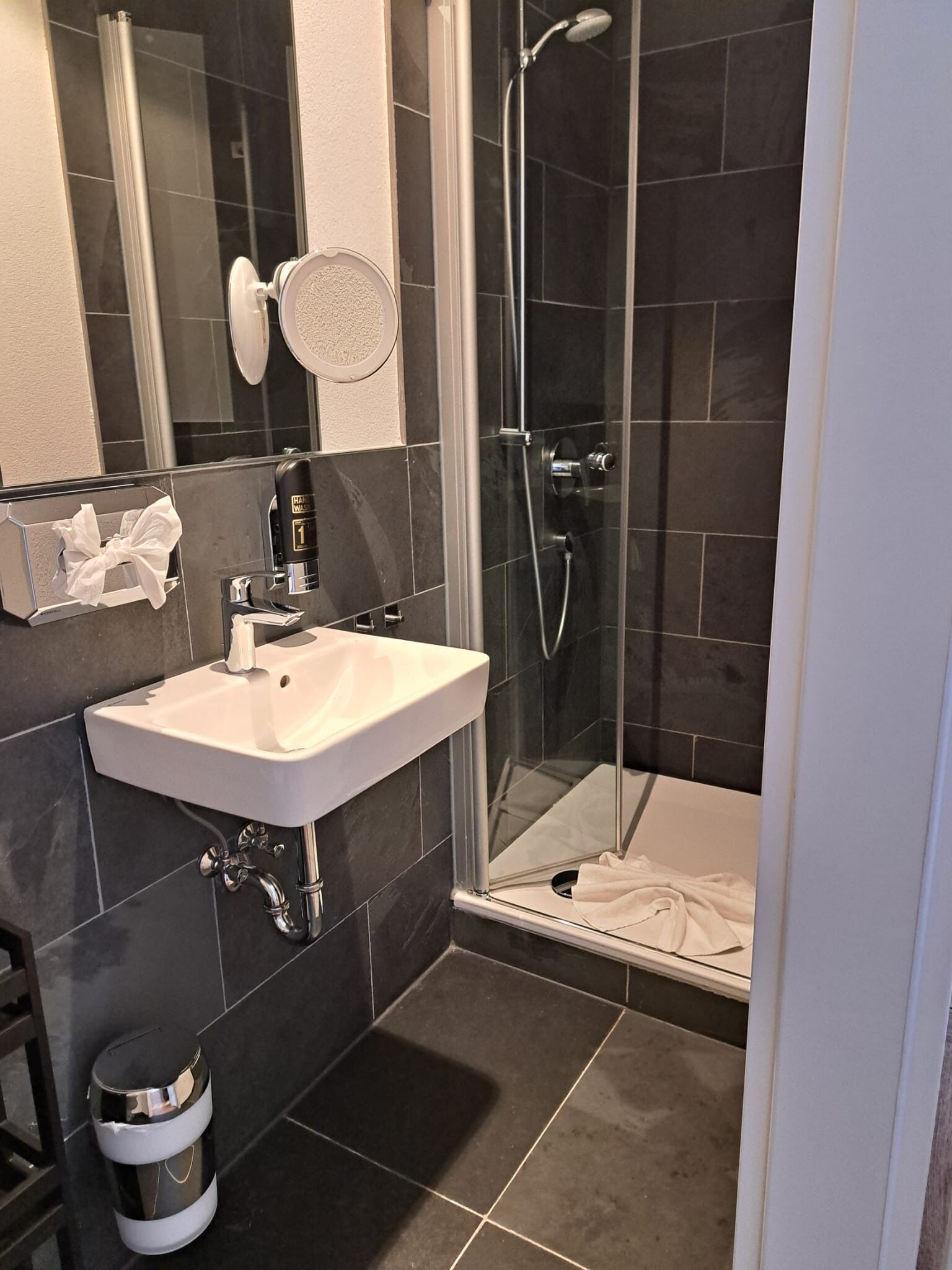 Un baño moderno con ducha de vidrio, lavamanos blanco y perchero.