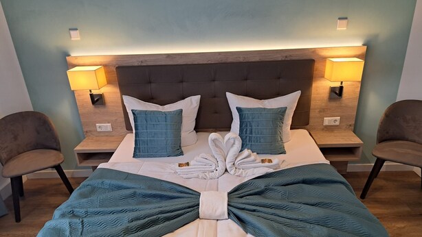 A neatly made bed with a towel arrangement, two bedside tables with lamps, and two chairs. - VILLAWIE  (Rheda-Wiedenbrück)
