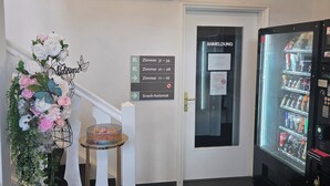 A hotel entrance with a sign reading 'Villawie,' a welcome sign, directional signs to rooms 11-16, 21-26, and 31-34, a snack-automat, and a vending machine. - VILLAWIE  (Rheda-Wiedenbrück)
