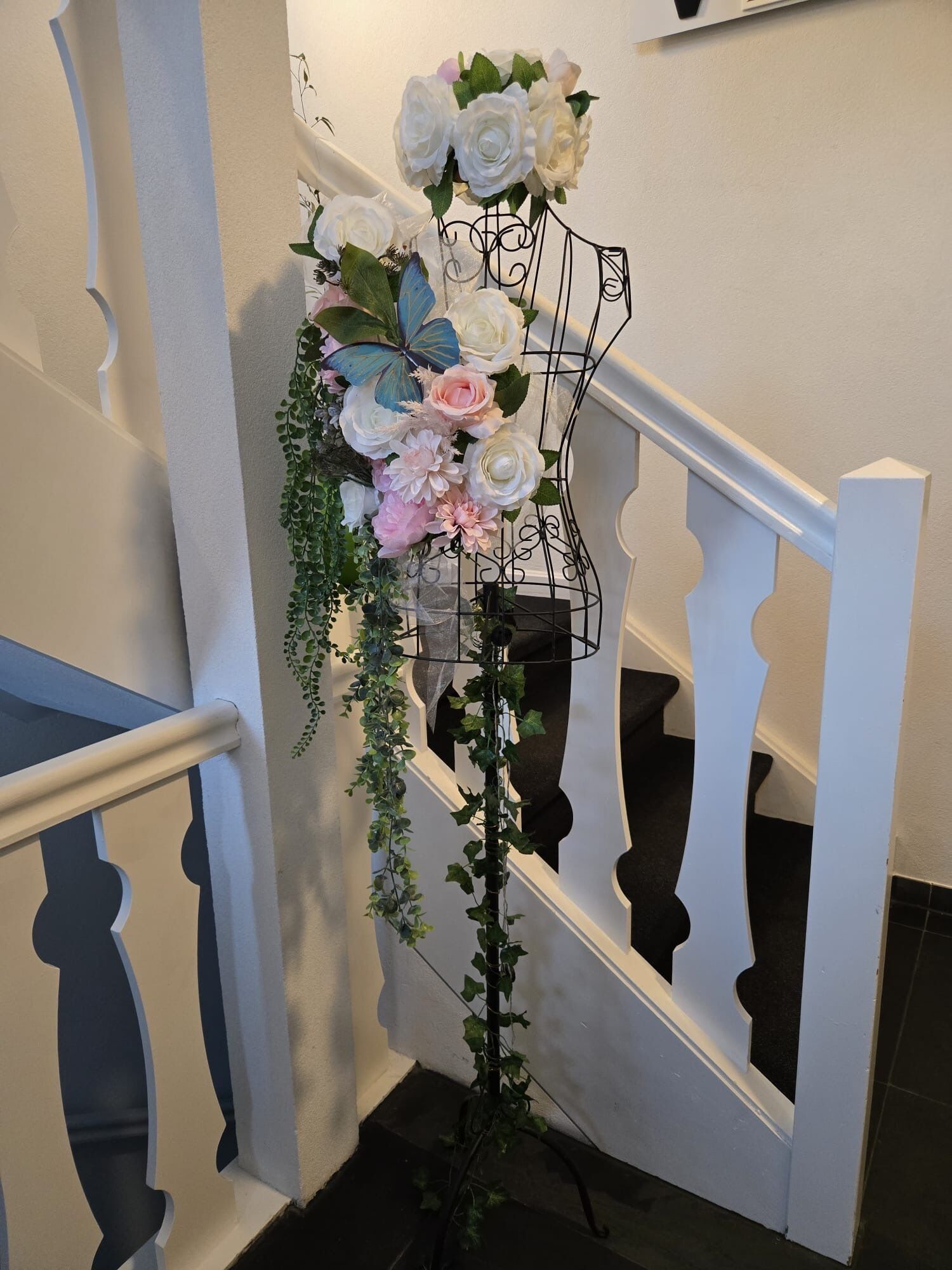 A staircase with a white railing and a floral arrangement on a stand.