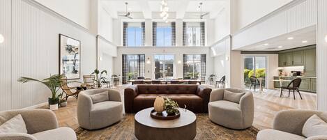 A spacious lobby with a central seating area, a kitchen in the background, and large windows.