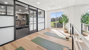 Ein moderner Fitnessraum mit Trainingsgeräten, Holzböden und großen Fenstern.