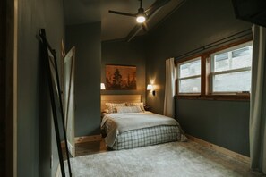 Une chambre à coucher avec un lit, un ventilateur de plafond, un tableau, une fenêtre et une table de chevet.