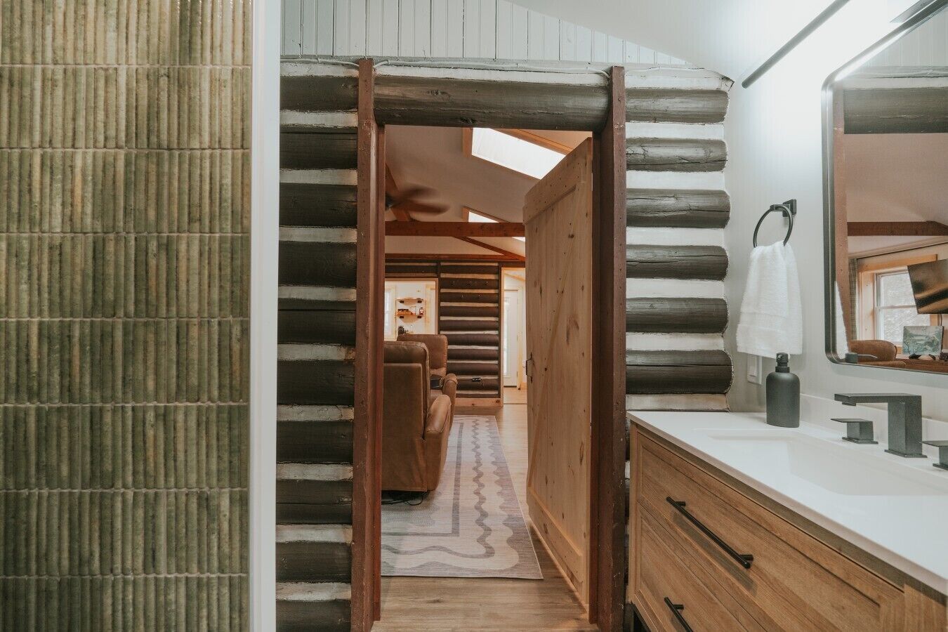 Ein Blockhaus-Innenraum mit Holztür, einem Badezimmer mit Spiegel und einem Flur, der zum Schlafzimmer führt.