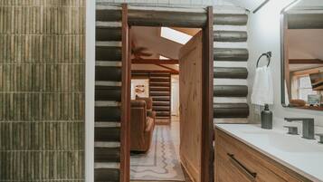 Ein Blockhaus-Innenraum mit Holztür, einem Badezimmer mit Spiegel und einem Flur, der zum Schlafzimmer führt.