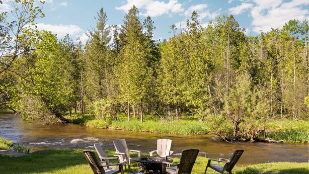 A riverside outdoor seating area with chairs and a table, surrounded by trees. - Platte River Sauna, Hot Tub & Kayaks, Near Dunes (Honor)
