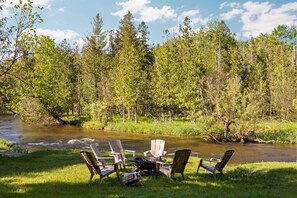 A riverside outdoor seating area with chairs and a table, surrounded by trees. - Platte River Sauna, Hot Tub & Kayaks, Near Dunes (Honor)