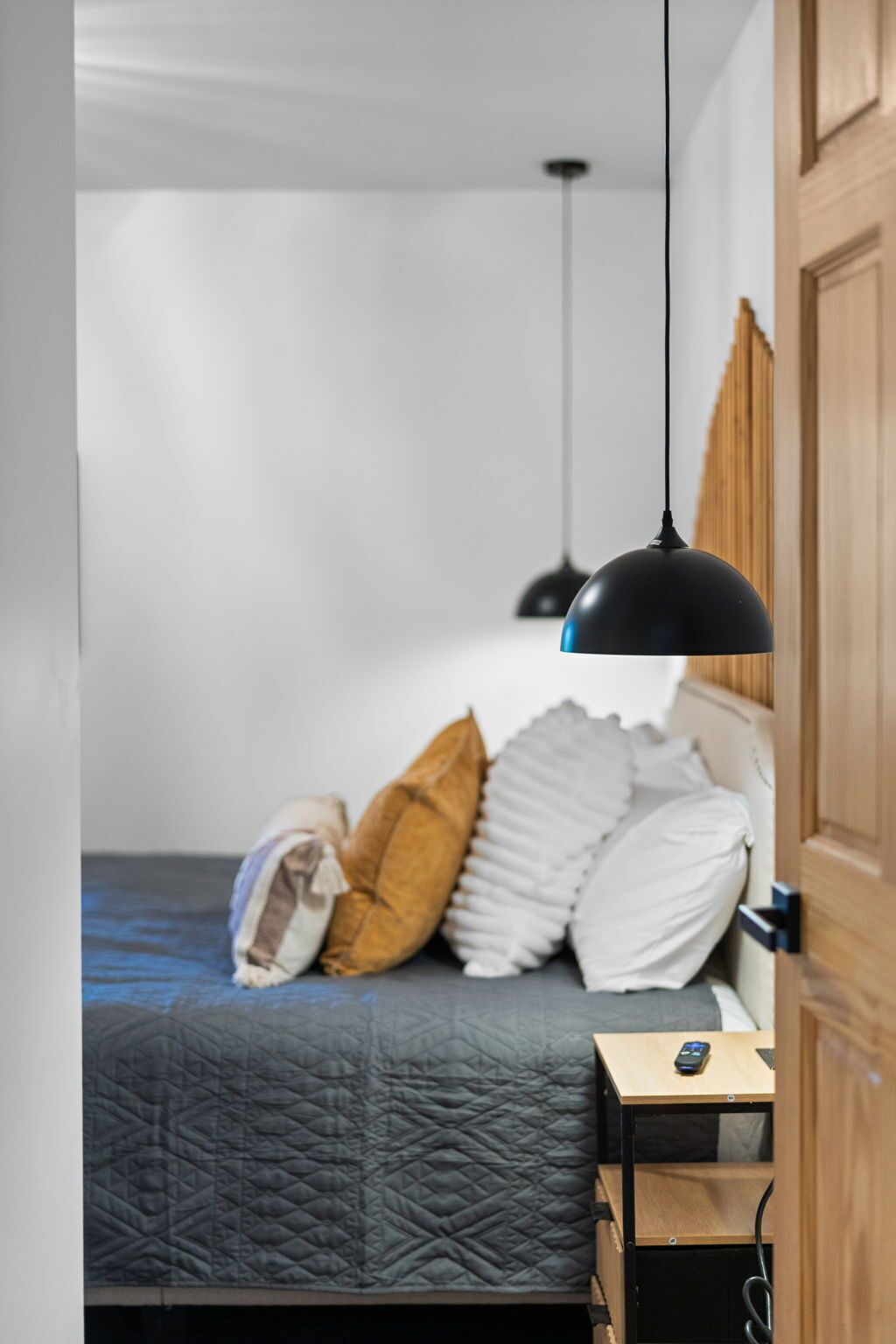 Un dormitorio con cama, almohadas, una colcha acolchada, una mesita de noche con teléfono y una lámpara colgante.