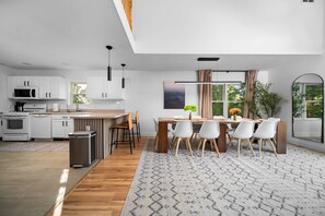 Een moderne keuken met witte kastjes, een houten eettafel en uitzicht op groen.