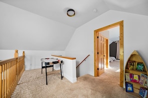 A room with a sloped ceiling, a wooden door, a small table with a chair, and a bookshelf. - Platte River Sauna, Hot Tub & Kayaks, Near Dunes (Honor)