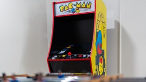 A Pac-Man arcade machine with a red top and yellow sides, featuring the game's logo and character. - Platte River Sauna, Hot Tub & Kayaks, Near Dunes (Honor)