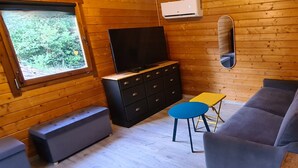 A wooden cabin interior with a sofa, a TV on a dresser, a small table, and a bench. - Charming wooden chalet - Ardèche (Joyeuse)
