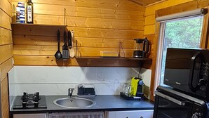 A compact kitchen with wooden walls, a gas stove, a sink, a microwave, and a window. - Charming wooden chalet - Ardèche (Joyeuse)