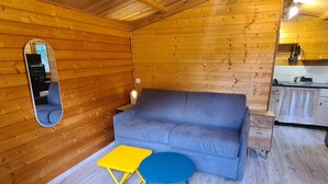 A wooden interior with a sofa, a small table, a mirror, and a kitchen area. - Charming wooden chalet - Ardèche (Joyeuse)