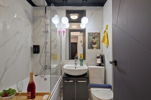 Un baño moderno con ducha envuelta en vidrio, un lavabo blanco, un inodoro y un tocador con espejo. Hay tres lámparas colgantes sobre el lavabo y una toalla colgada en la pared.