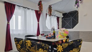A dining area with a table set for two, featuring a bottle of wine, glasses, and a basket of snacks. The chairs have a tropical leaf pattern. - Nova City View+ Near Hospital+Full Kitchen+A/C+Free Public Parking (Bucharest)