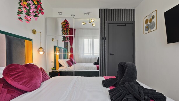 A modern hotel room with a large bed, a vanity with a mirror, and a hanging floral arrangement. - Nova City View+ Near Hospital+Full Kitchen+A/C+Free Public Parking (Bucharest)