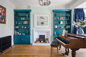Una sala de estar con estanterías color turquesa, chimenea, piano y radiador.