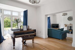 Een woonkamer met een vleugelpiano, een bank, een televisie en een open haard.