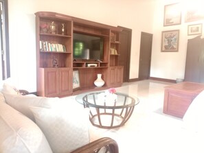 A living room with a sofa, a glass coffee table, a television, wooden shelving with books and decorative items, and framed pictures on the wall. - Vrbo Property (La Romana)