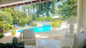 A poolside area with a white sofa, lounge chairs, and a table with a plant. - Coral Suite at Casa de Campo Resort & Villas Golf Playa (La Romana)