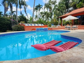 A swimming pool with tiled edges, lounge chairs, and palm trees in the background. - Vrbo Property (La Romana)