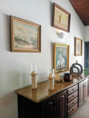 A kitchen with granite countertops, dark wooden cabinets, and framed artwork on the wall.