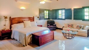 A spacious room with a large bed, a sofa, a chair, a small table, and a ceiling fan. - Coral Suite at Casa de Campo Resort & Villas Golf Playa (La Romana)
