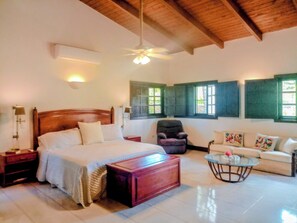 A spacious room with a large bed, a sofa, a chair, a small table, and a ceiling fan. - Vrbo Property (La Romana)