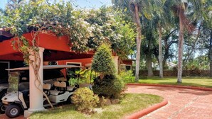 A paved driveway leading to a building with a golf cart parked under a tree. - Coral Suite at Casa de Campo Resort & Villas Golf Playa (La Romana)