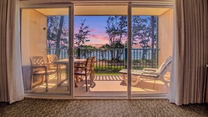 A room with a sliding glass door leading to an outdoor seating area with a table and chairs, and a view of trees and a body of water. - Barefoot Beach Escape Pono Kai Resort  D207 (Kapaʻa)