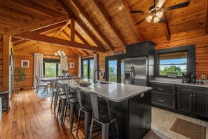 A wooden cabin interior with a kitchen, dining area, and bar stools. - Golf Simulator Cabin With Big Smoky Views (Sevierville)