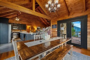 A spacious kitchen with a central island, wooden ceiling beams, and a dining area with a large table and benches. - Golf Simulator Cabin With Big Smoky Views (Sevierville)