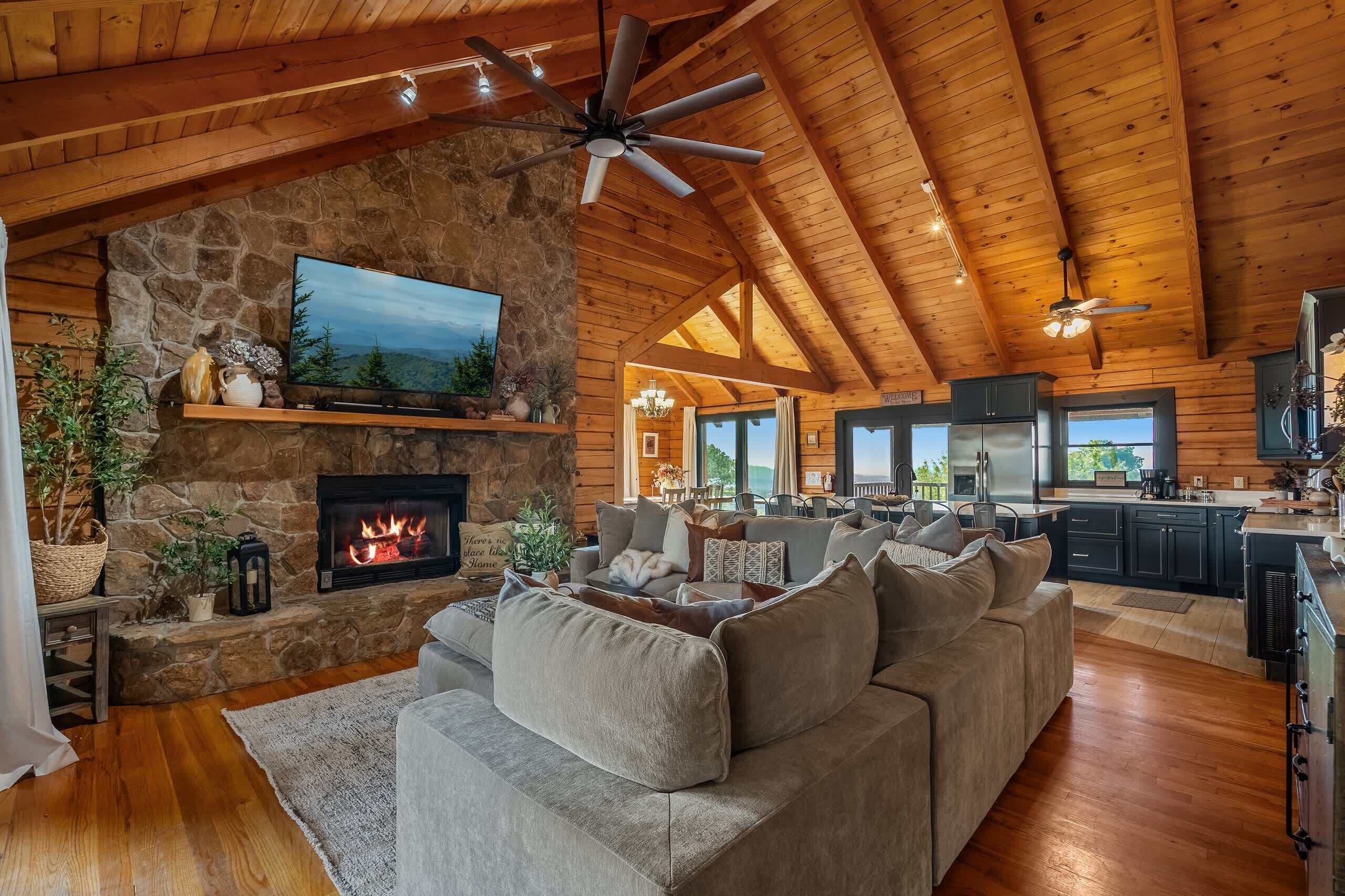 A spacious living area with a stone fireplace, a large sofa, and a television mounted on the wall.