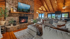 A cozy living room with a stone fireplace, a television mounted on the wall, and a ceiling fan. - *New* Golf Sim Cabin | Views | Hot Tub | Fire Pit (Sevierville)
