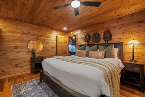 Une chambre à coucher aux murs lambrés, avec un lit, des tables de chevet, un miroir et un ventilateur de plafond.