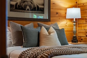 A bed with multiple pillows and a blanket, a wooden wall, a framed picture, and a lamp. - Golf Simulator Cabin With Big Smoky Views (Sevierville)