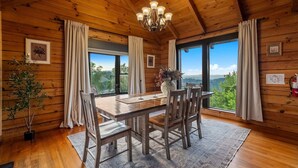 A wooden cabin interior with a dining table, chairs, a chandelier, and large windows offering a view of the outdoors. - *New* Golf Sim Cabin | Views | Hot Tub | Fire Pit (Sevierville)