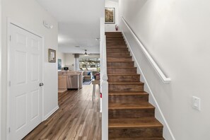 Eine Treppe mit Holzboden und weißen Geländern, die zu einem Raum mit einer weißen Tür und einem Deckenventilator führt.