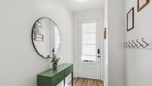 A hallway with a green console table, a round mirror with a decorative frame, a white door with frosted glass panels, and a wall-mounted coat rack. - Gorgeous 3/3 townhome at gated Resort Community at Windsor Palms!! (Kissimmee)