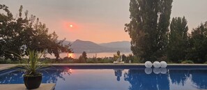 A serene pool area with a Buddha statue, surrounded by trees and a view of mountains. - Naramata Vineyard . Saltwater Pool . Walk to Wineries (Naramata)