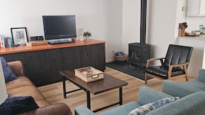 Ett vardagsrum med en soffa, ett soffbord, en tv, en öppen spis och en köksdel.