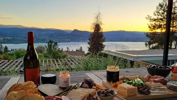 En picknickuppsättning med olika sorters mat och en flaska på ett träbord, med en vacker utsikt som bakgrund.