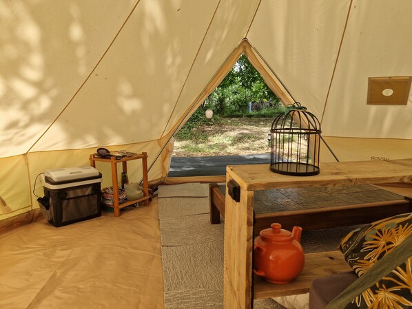 A tent interior with a table, a small stool, a storage box, and a birdcage.