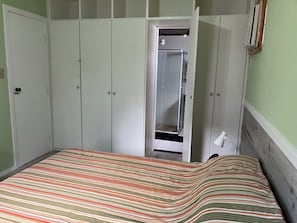 A bedroom with a bed, a wardrobe, and a shower area. - apart Queen barra (Salvador)
